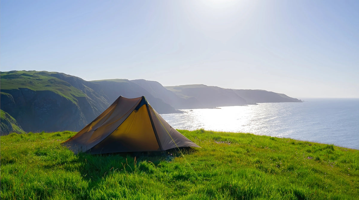 Khaki Lanshan 2 two-person trekking pole tent pitched on a grassy coastal hillside overlooking the ocean
