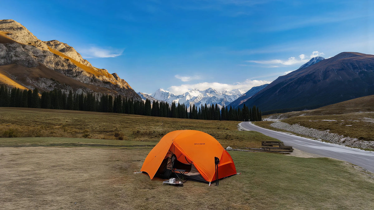 Orange 3F UL Gear Floating Cloud 2 freestanding tent pitched in a mountain meadow with snow-capped peaks in the background