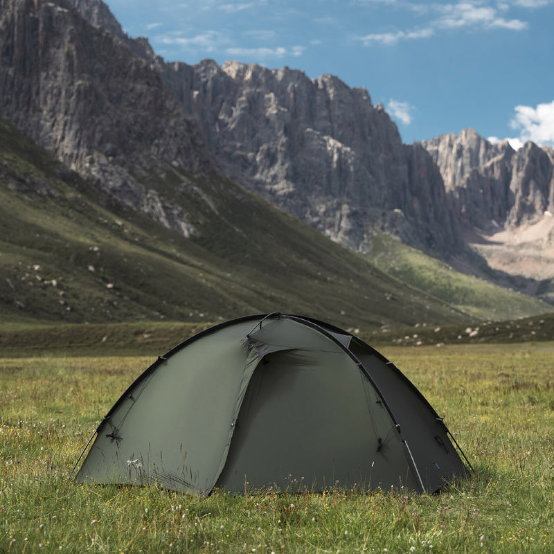 Pine green TFS Stars 2 Pro pitched on grass beneath rocky mountain cliffs.